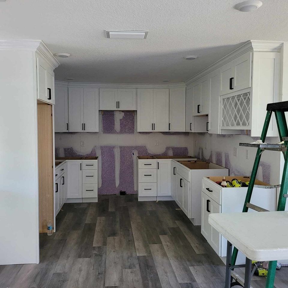 Kitchen remodel in progress with white cabinets, gray floors, and purple backing.