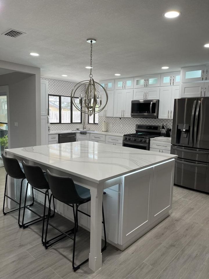 Modern white kitchen with island, seating, and stainless steel appliances.