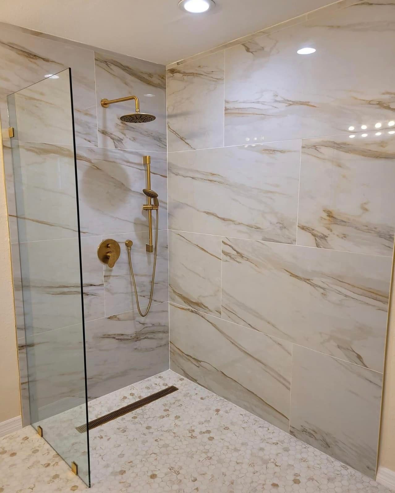 Modern shower with marble-like tile walls, gold fixtures, and glass enclosure. Pebble tile floor.