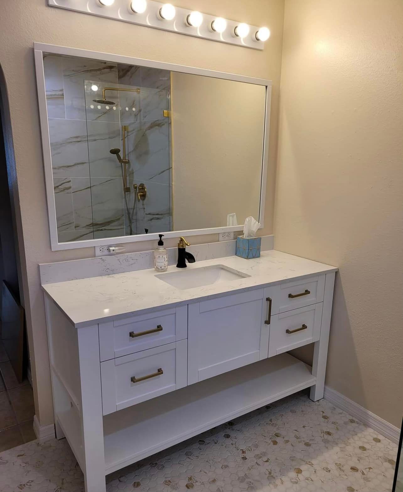 White bathroom vanity with marble countertop, large mirror, and gold fixtures.
