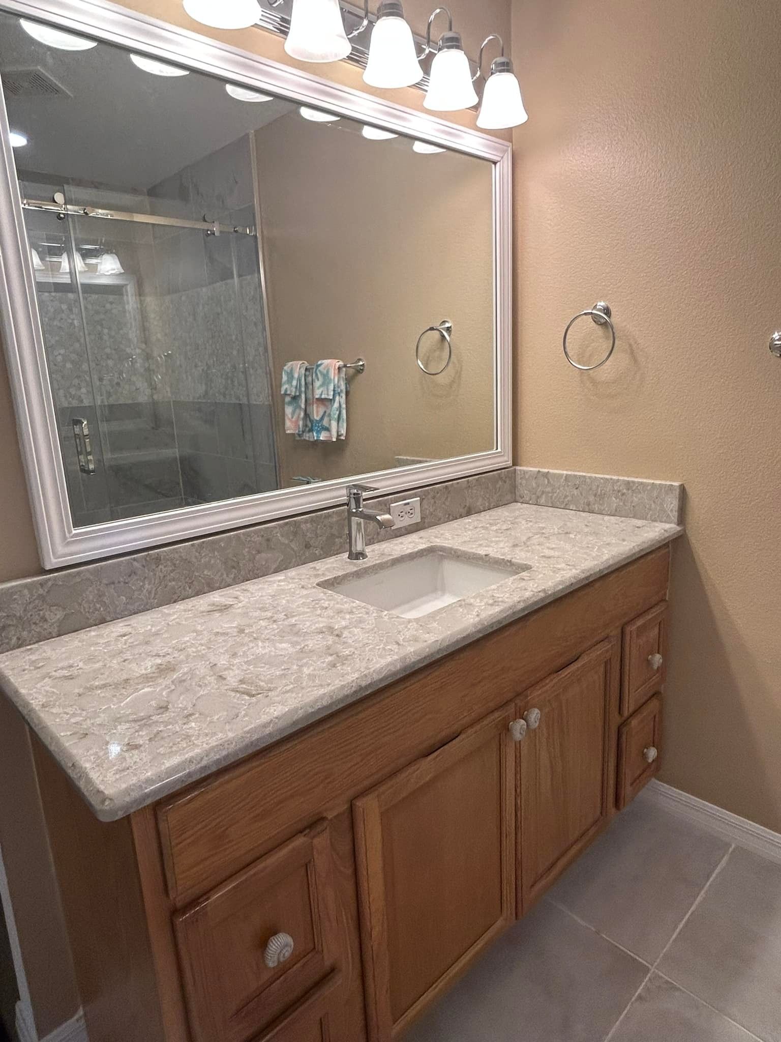 Bathroom vanity with light-colored countertop, light brown cabinets, large mirror, and recessed lighting.