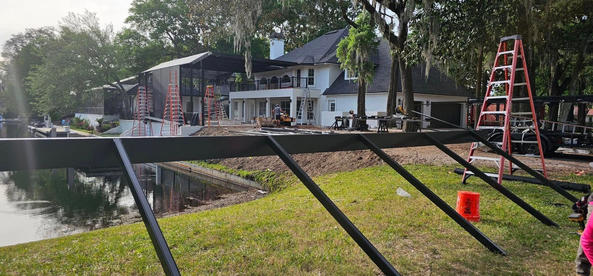 A white house with a burned-out section; construction equipment in the yard, near a lake.