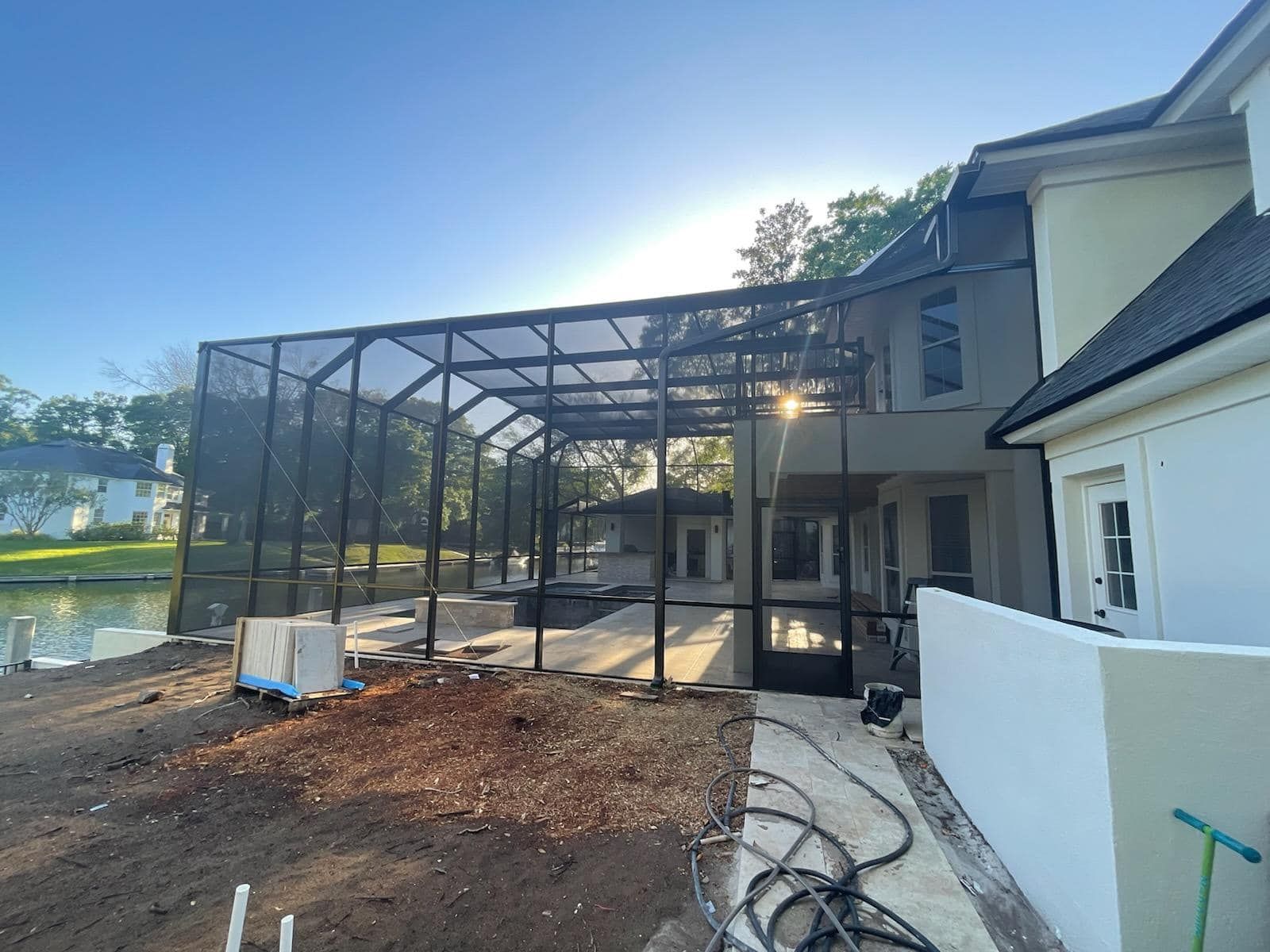 Pool enclosure under construction next to a house with a waterway view.