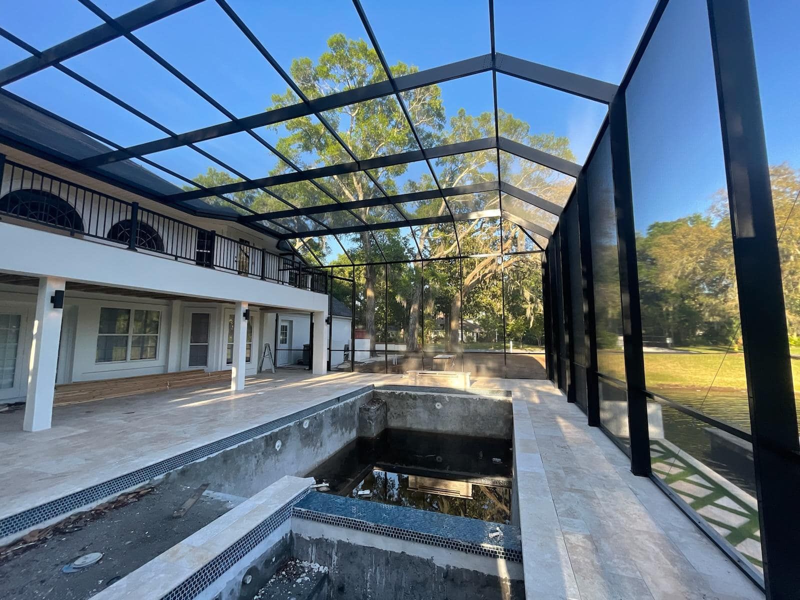 Pool area with glass enclosure and black metal frame, unfinished pool, sunny day.