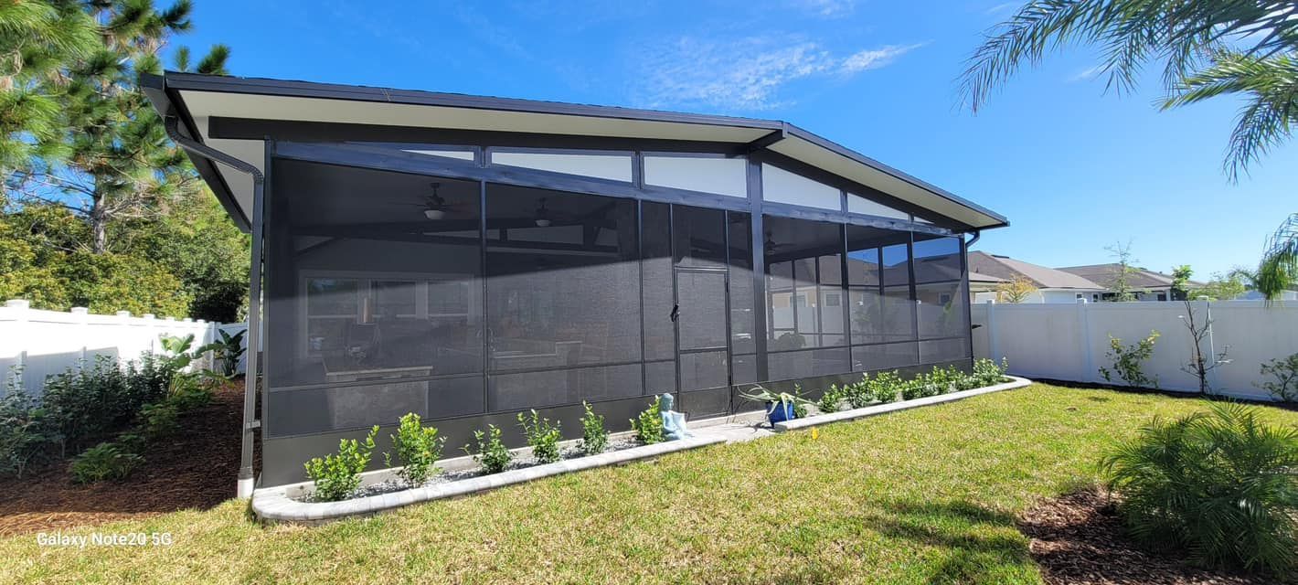 Screened-in patio with dark screening and a black roof, set in a grassy backyard with a white fence.