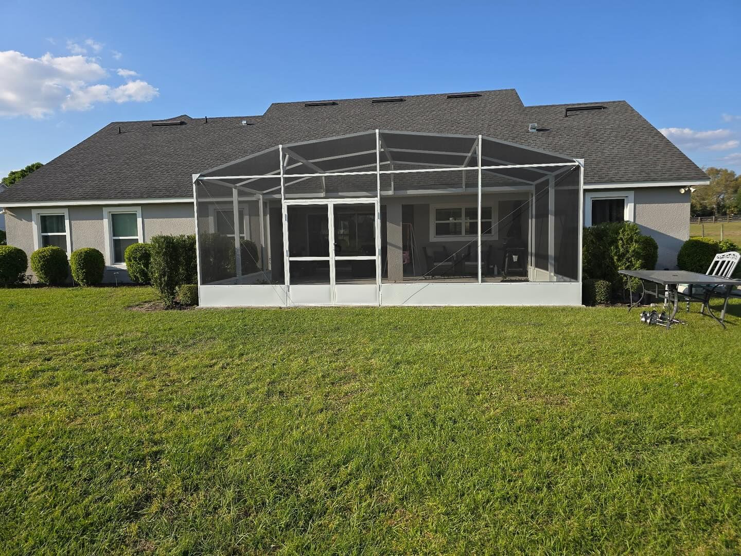 Back of a house with screened porch, surrounded by lawn. Blue sky.