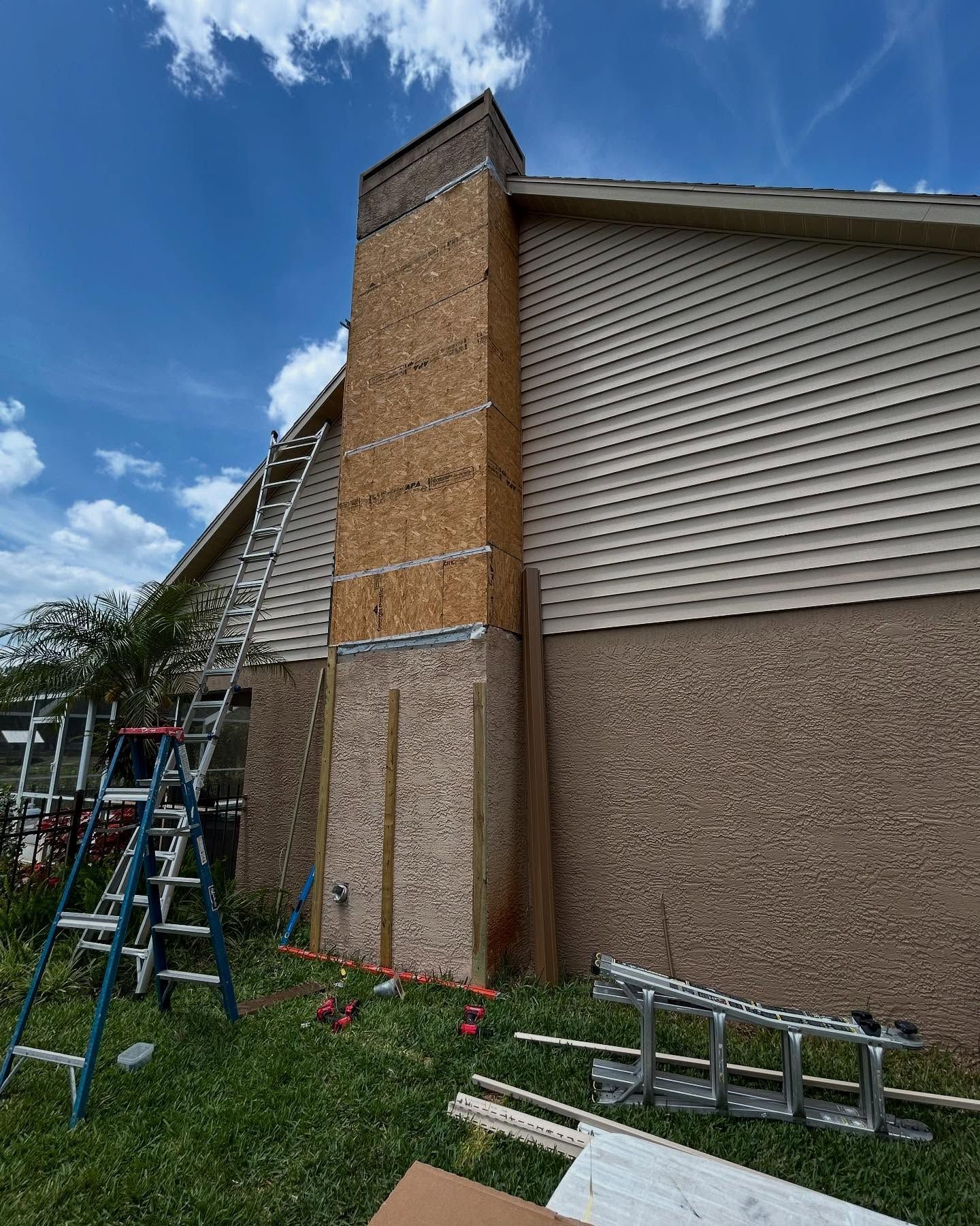 Chimney under construction next to a building, with exposed wood and ladders.