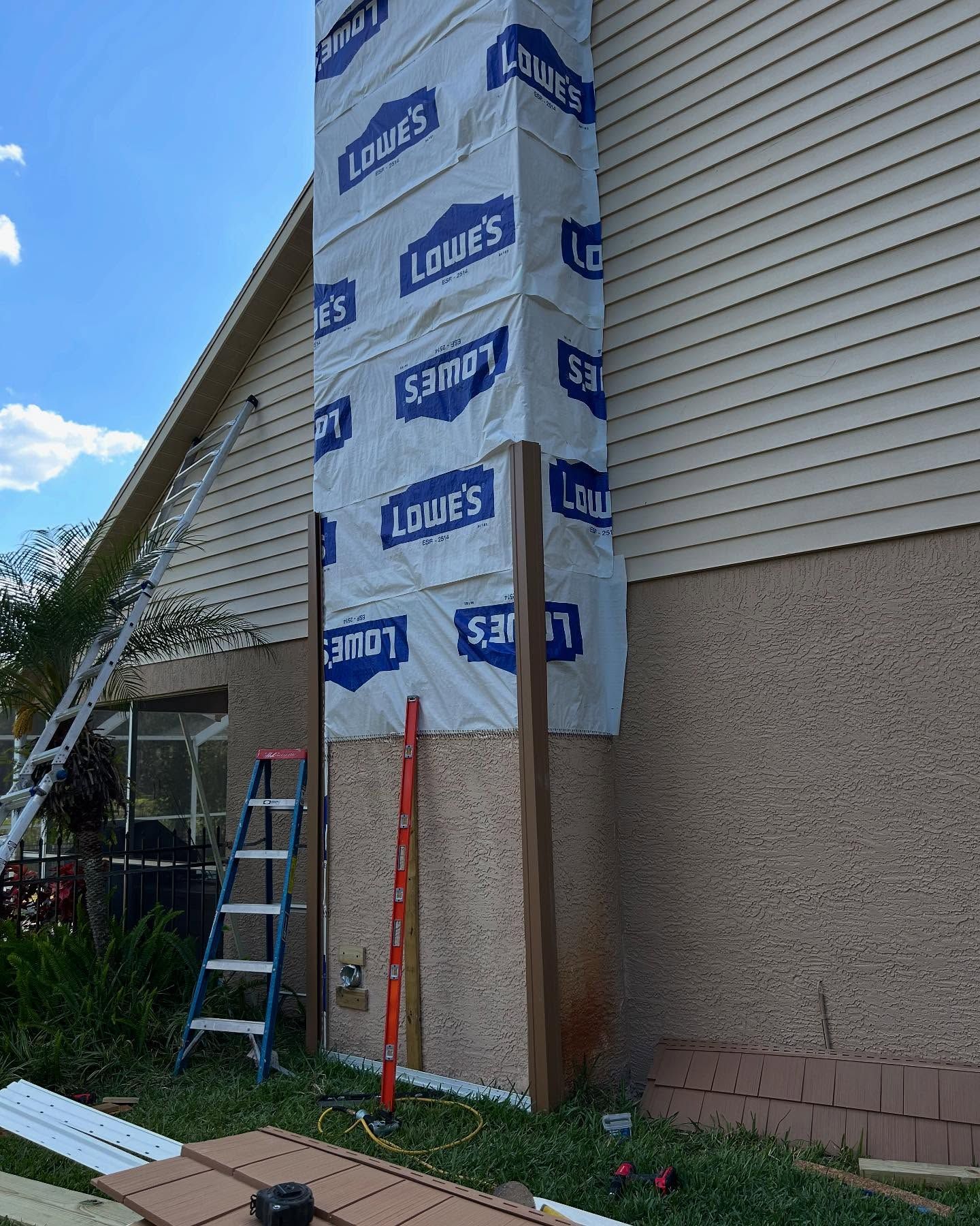 Chimney under construction wrapped in Lowe's paper, wooden beams, ladder, level, and house siding.
