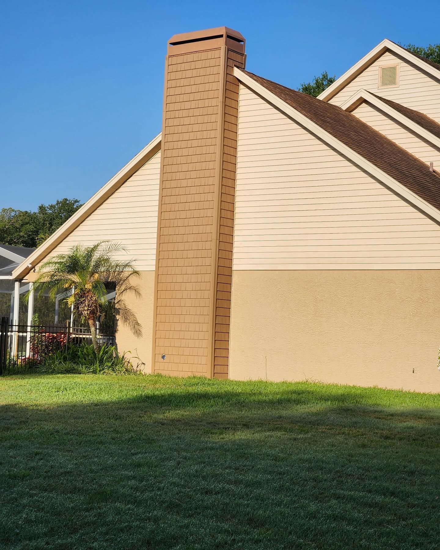 Tan brick chimney against a tan stucco wall and a light brown roof under a blue sky.