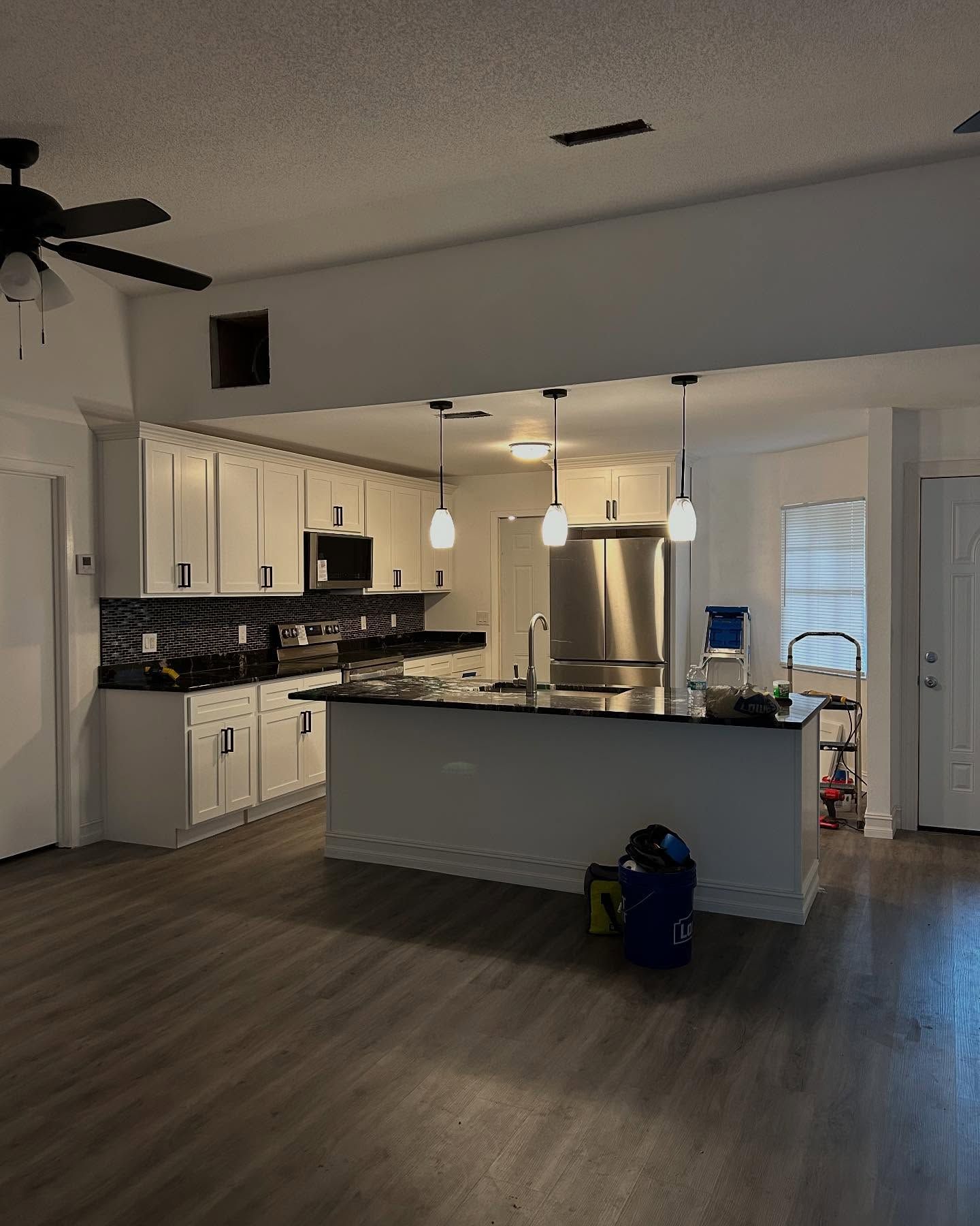 Open kitchen with white cabinets, dark countertops, and an island. Dark flooring, stainless steel fridge.