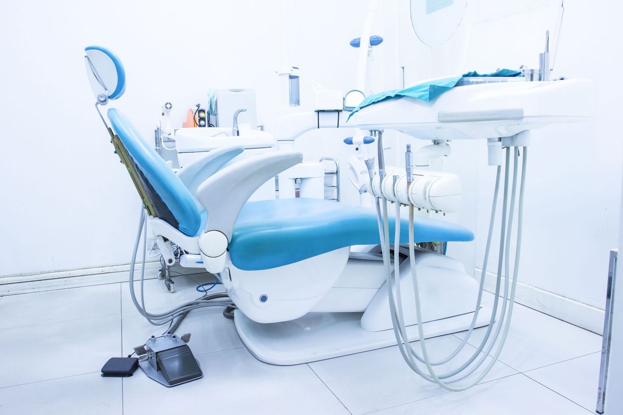 Blue and white dental chair in a bright, clinical setting. Dental tools are visible.