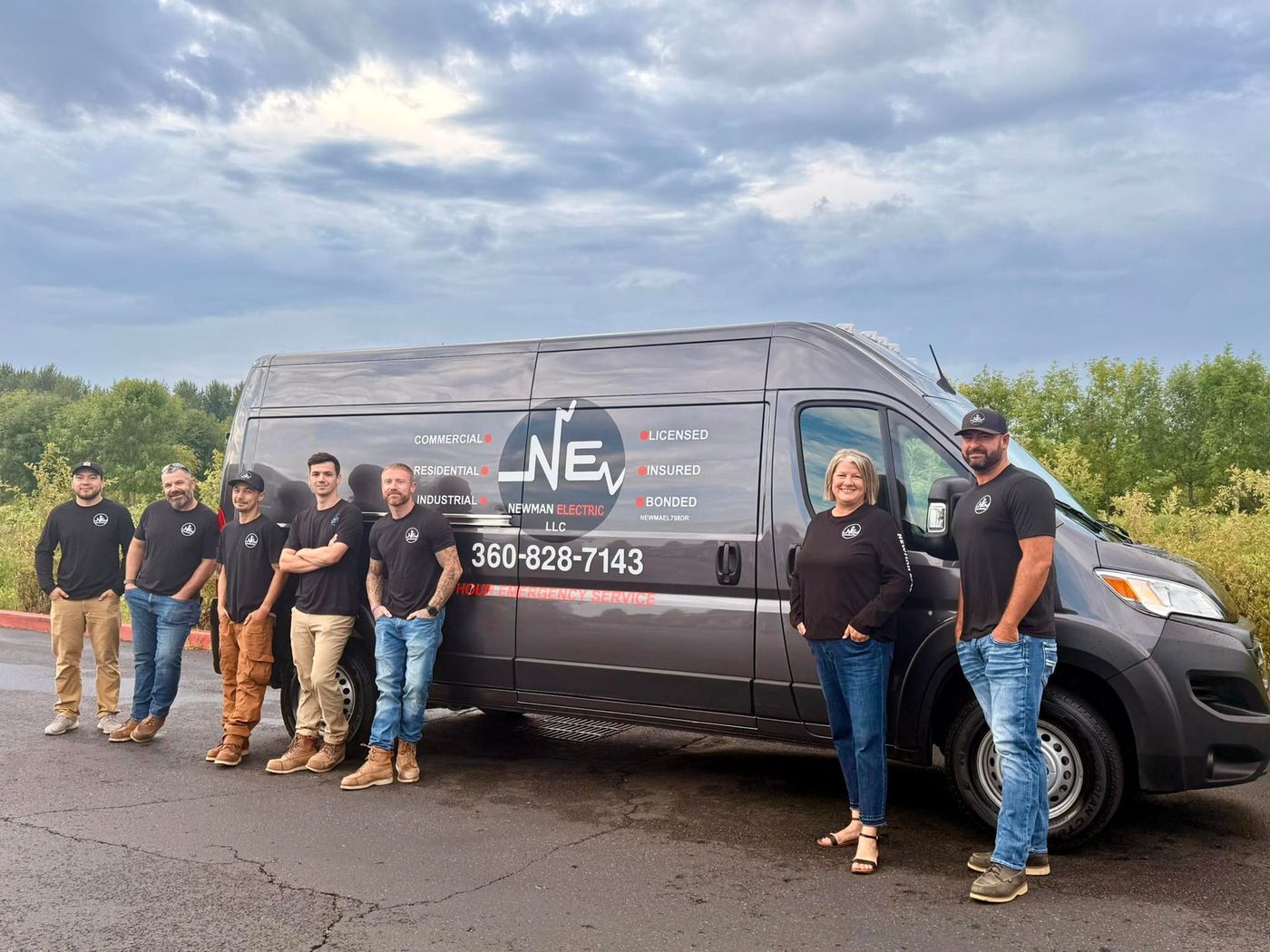 Group of workers in front of a black van with the company's logo. Cloudy day, outdoors.