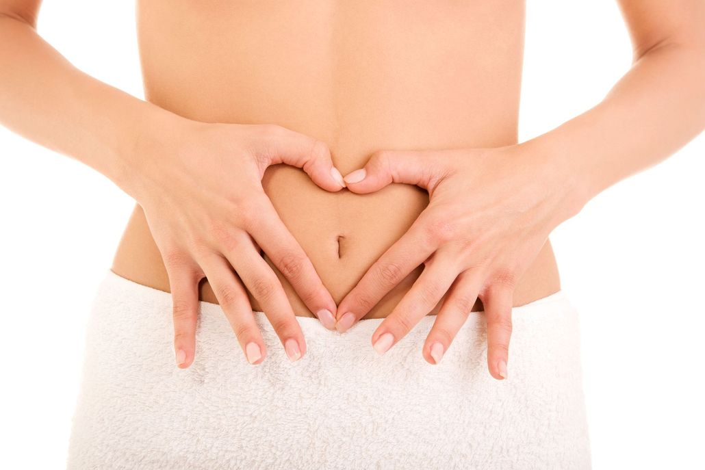 Hands forming a heart shape around a belly button on a person’s midriff, against a plain white background.