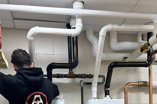 A man in a black hoodie is working on pipes in a room.