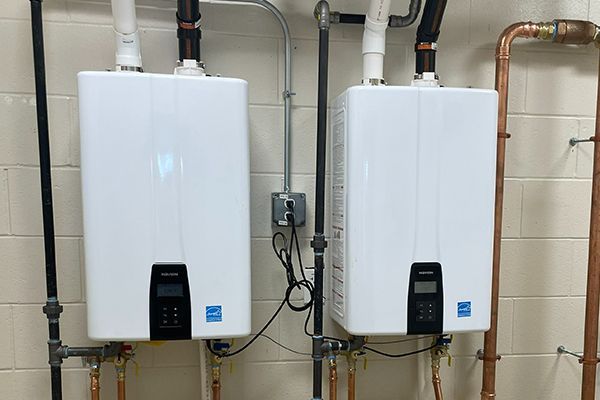 Two white water heaters are hanging on a wall next to copper pipes.