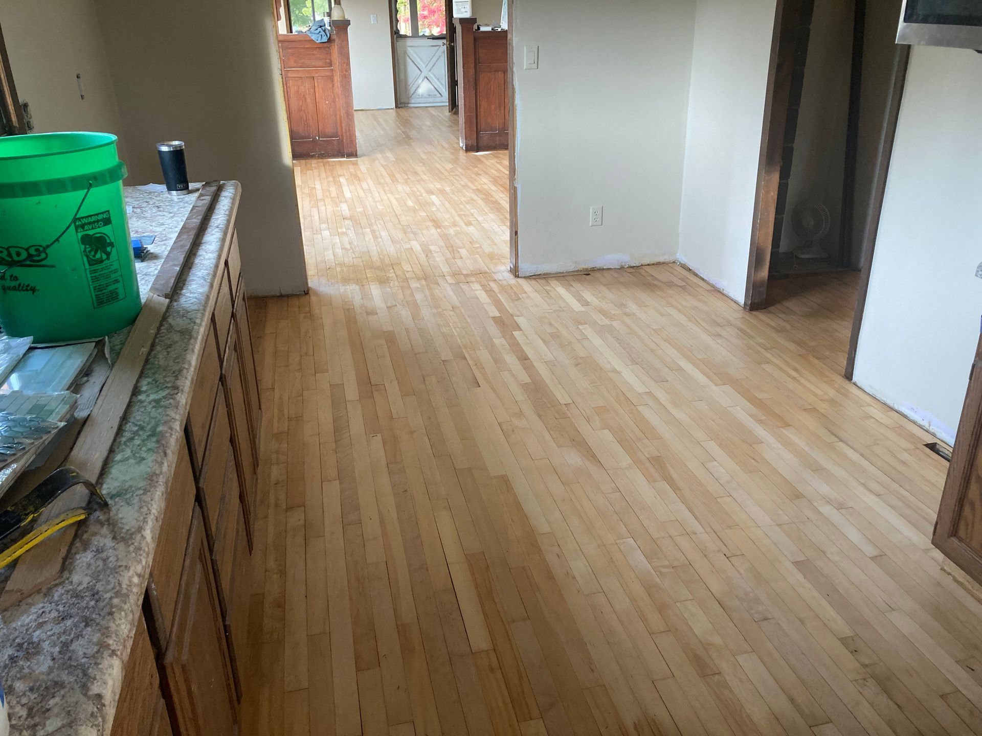 A kitchen with a wooden floor and a green bucket on the counter.