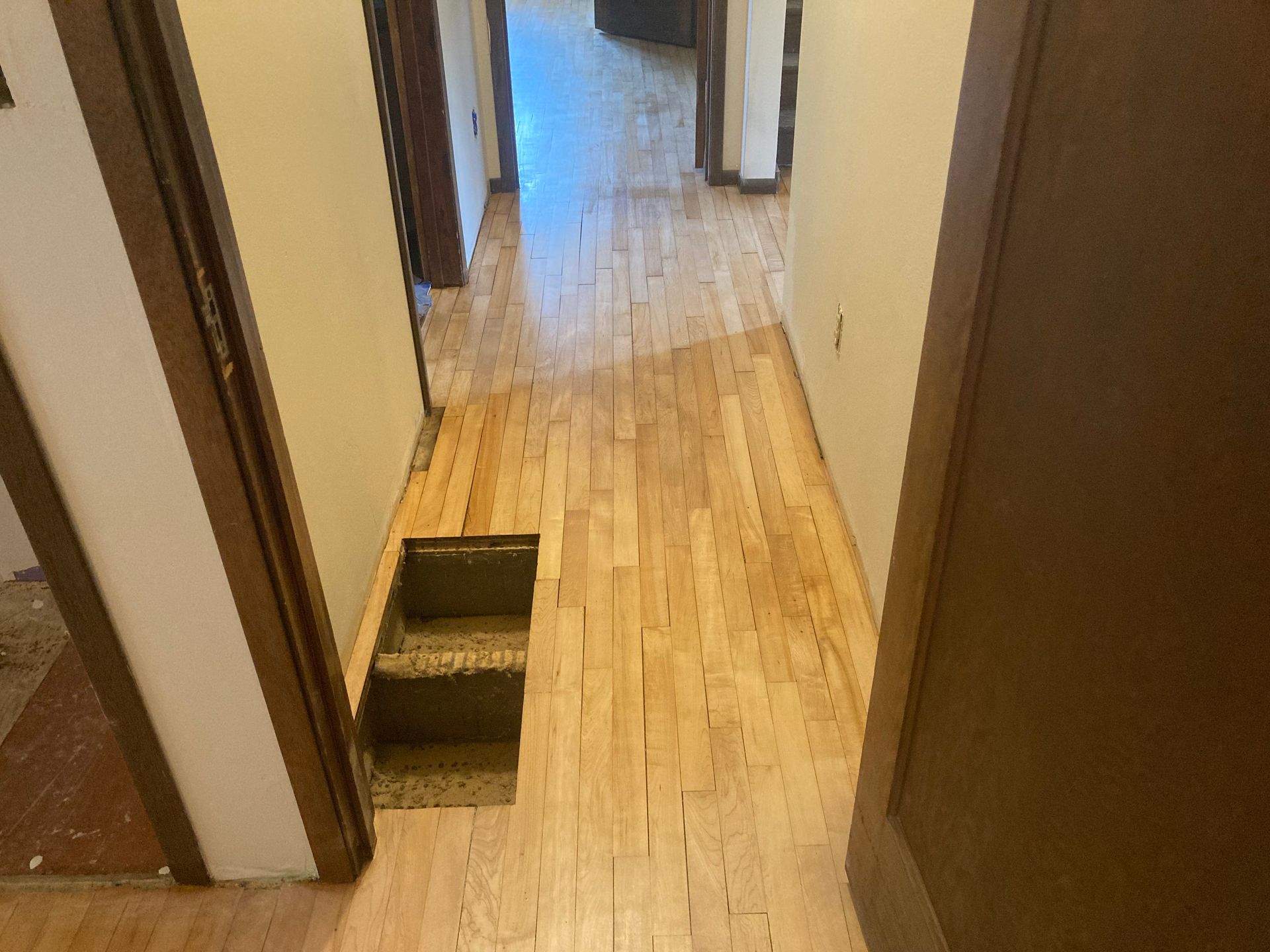 A hallway with hardwood floors and a hole in the floor.