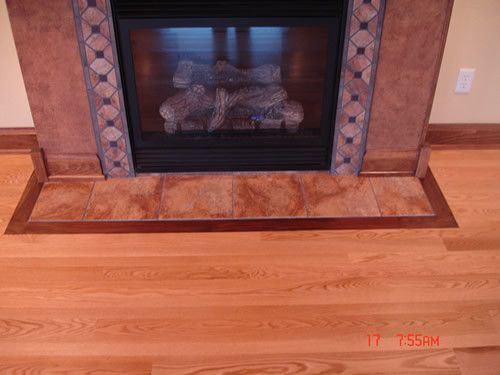 A fireplace with a tiled mantle and a wooden floor in a living room.