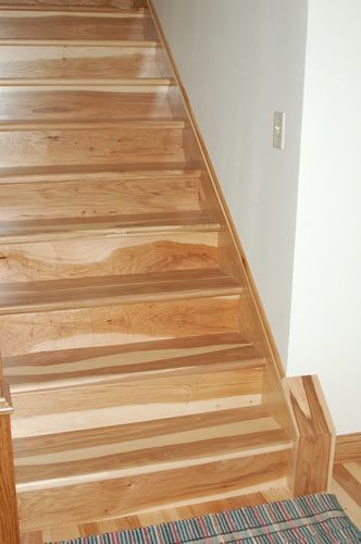 A close up of a wooden staircase with a rug on the floor.
