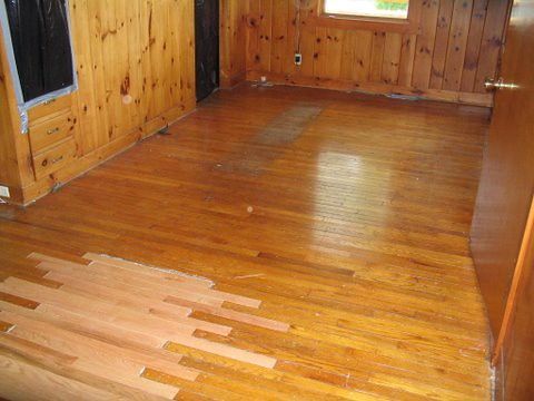 A wooden floor in a room with wood paneling and a window.