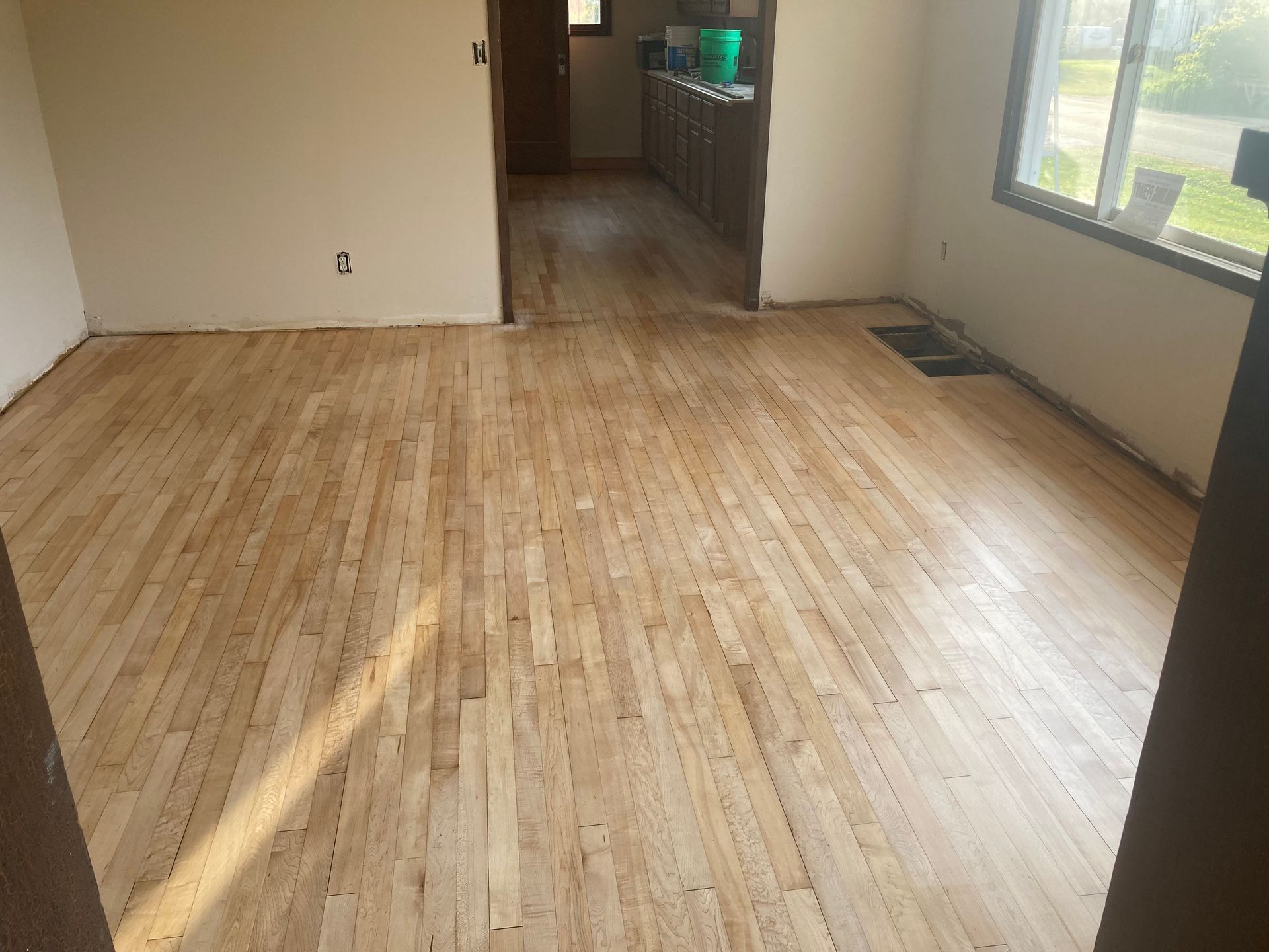 A living room with hardwood floors and a kitchen in the background.