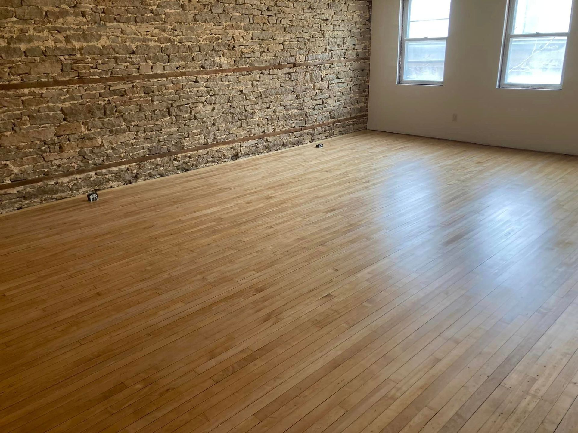An empty room with hardwood floors and a brick wall.