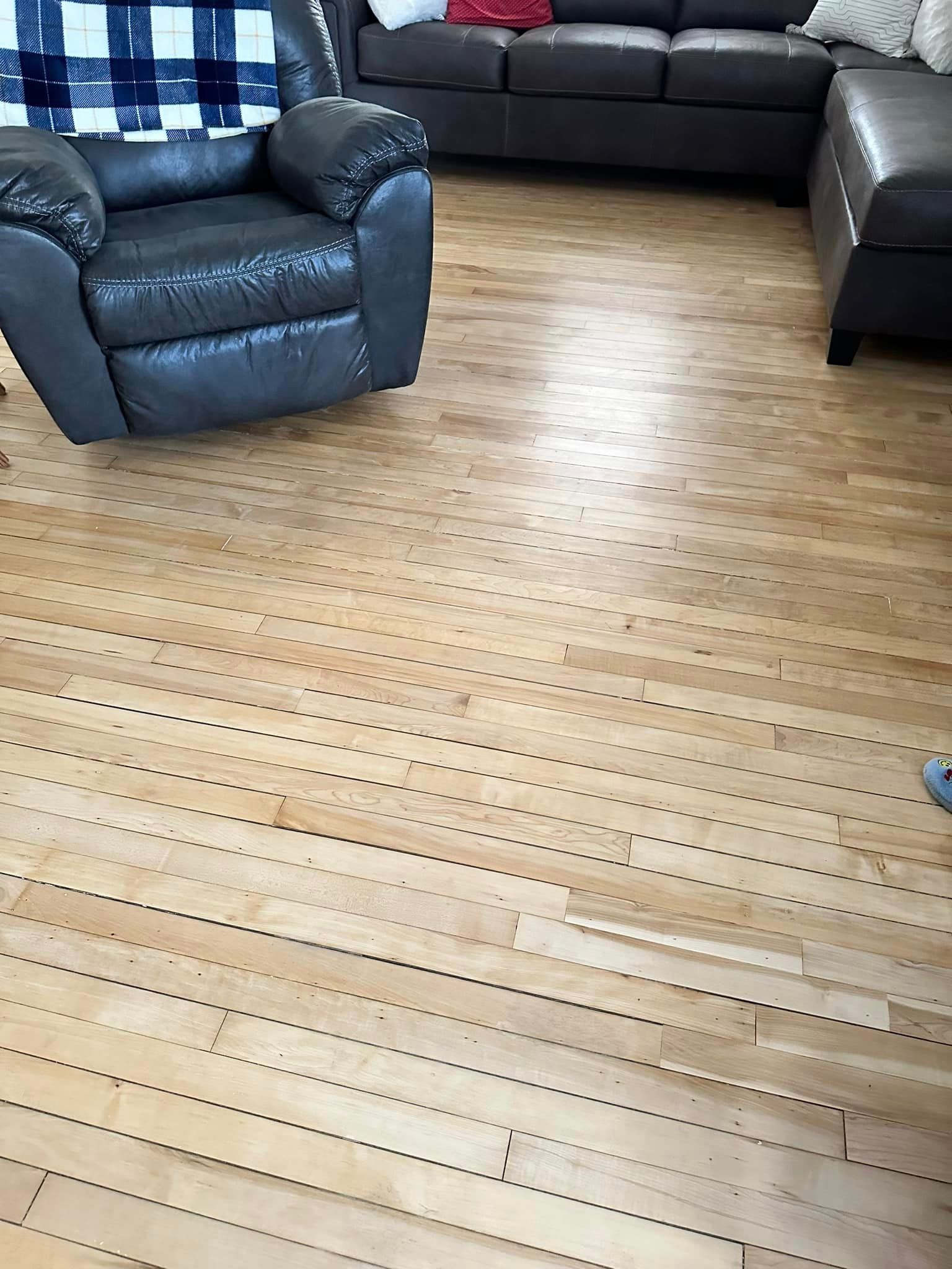A living room with a couch , chair , and ottoman on a wooden floor.