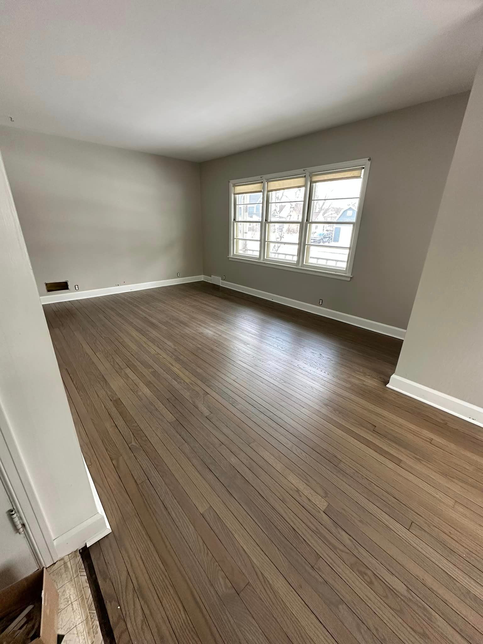 An empty living room with hardwood floors and two windows.
