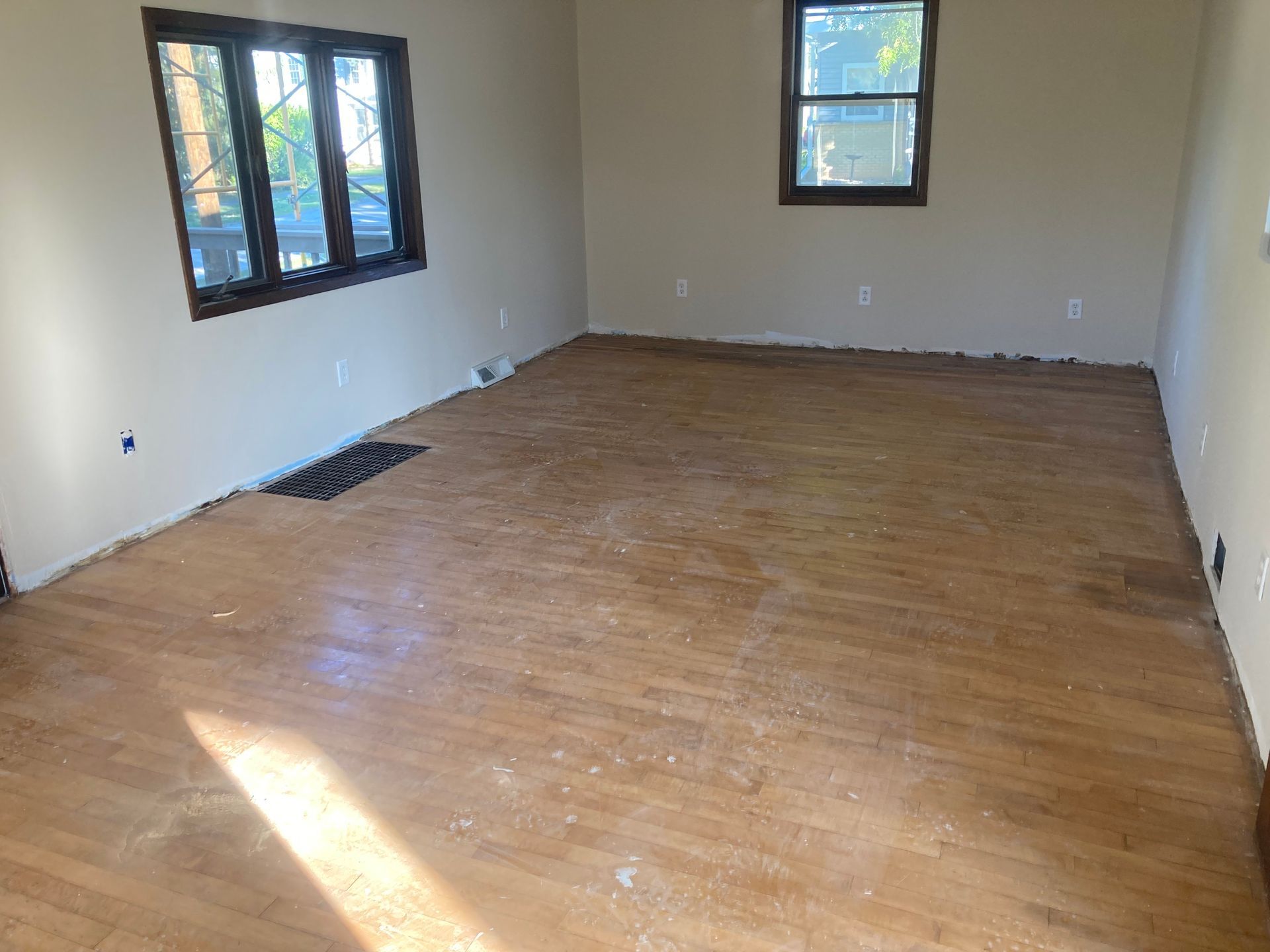 A large empty room with hardwood floors and two windows.
