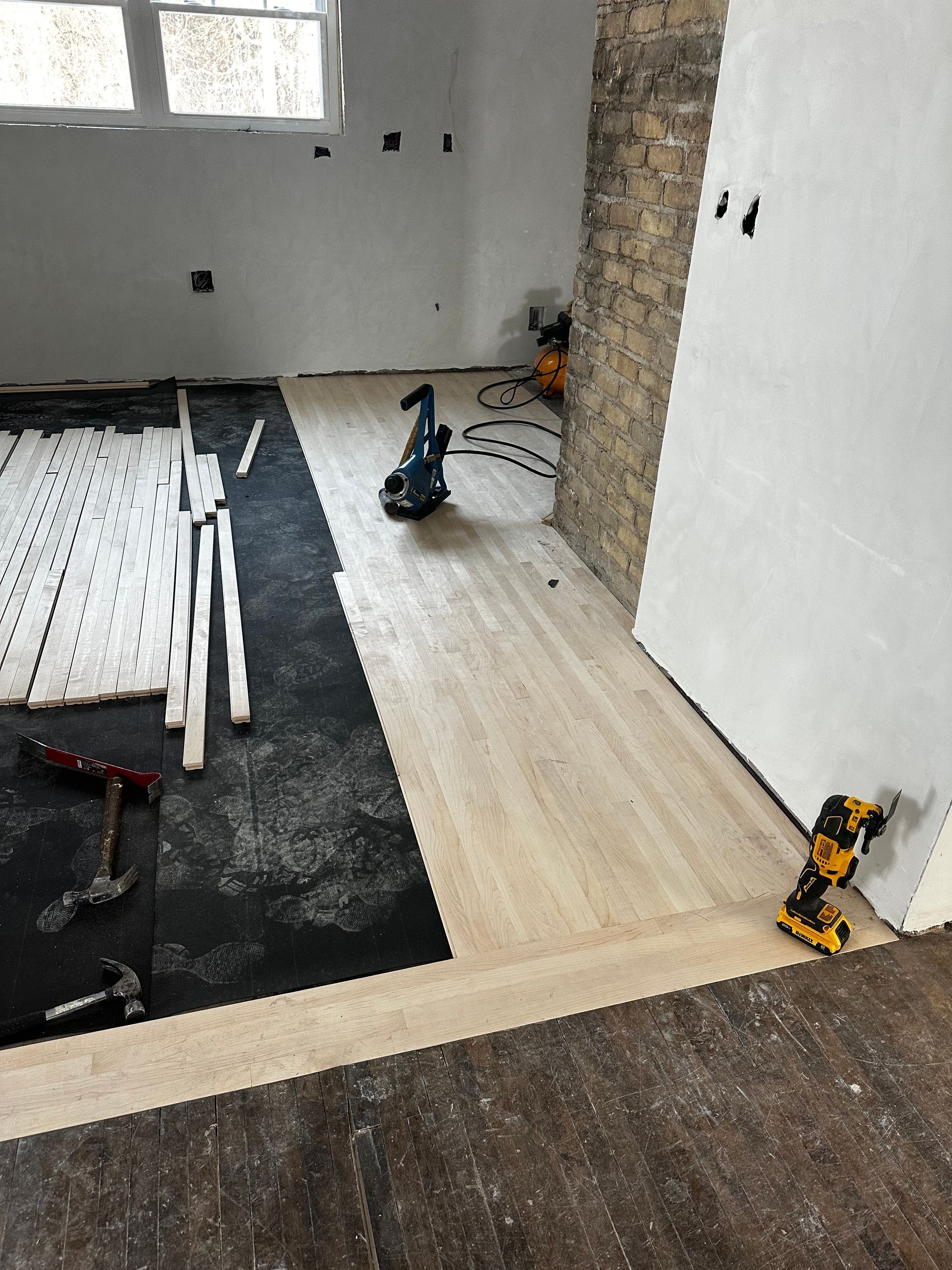 A room with a wooden floor and a drill on the floor.