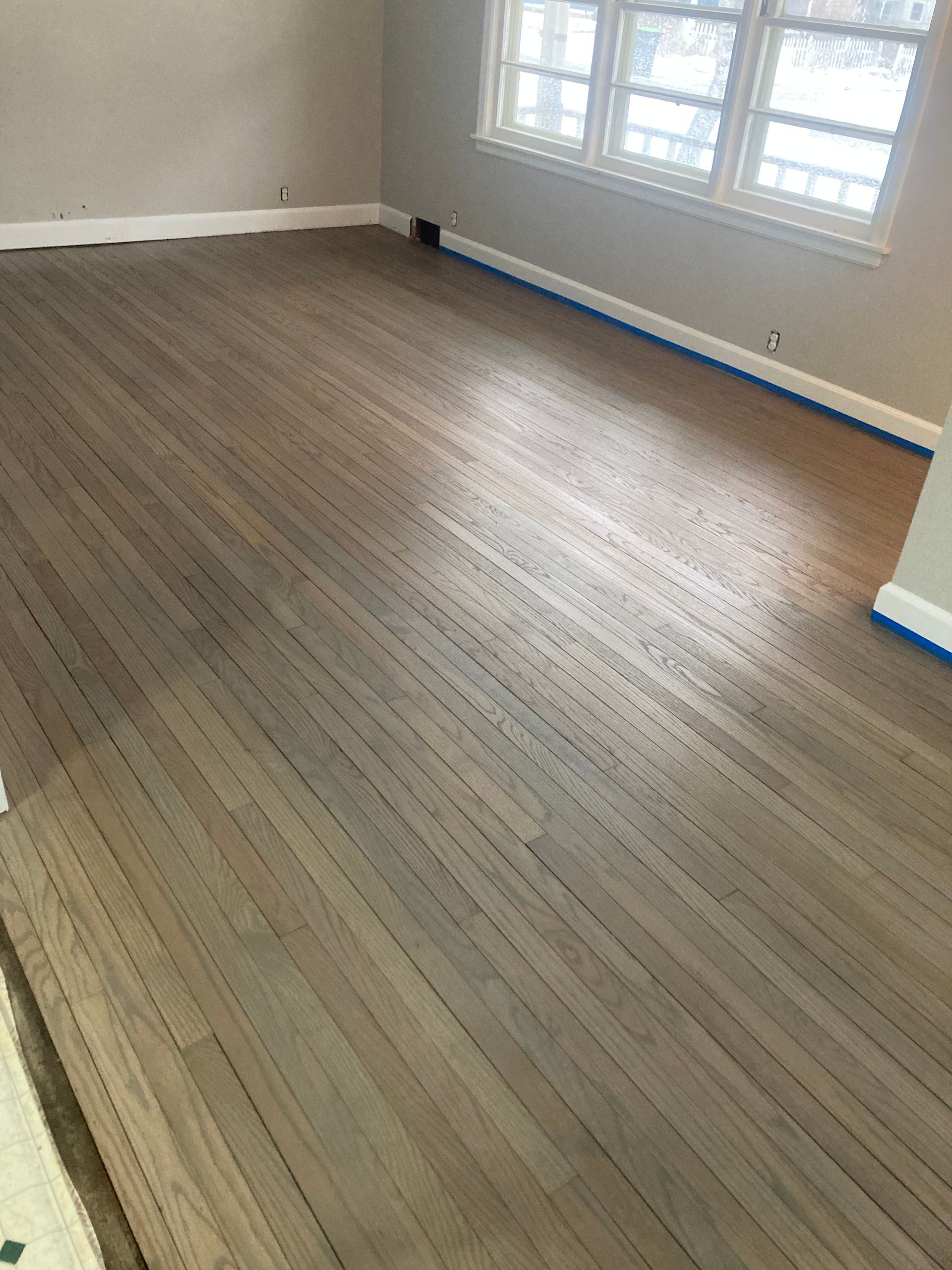 A living room with a wooden floor and two windows.