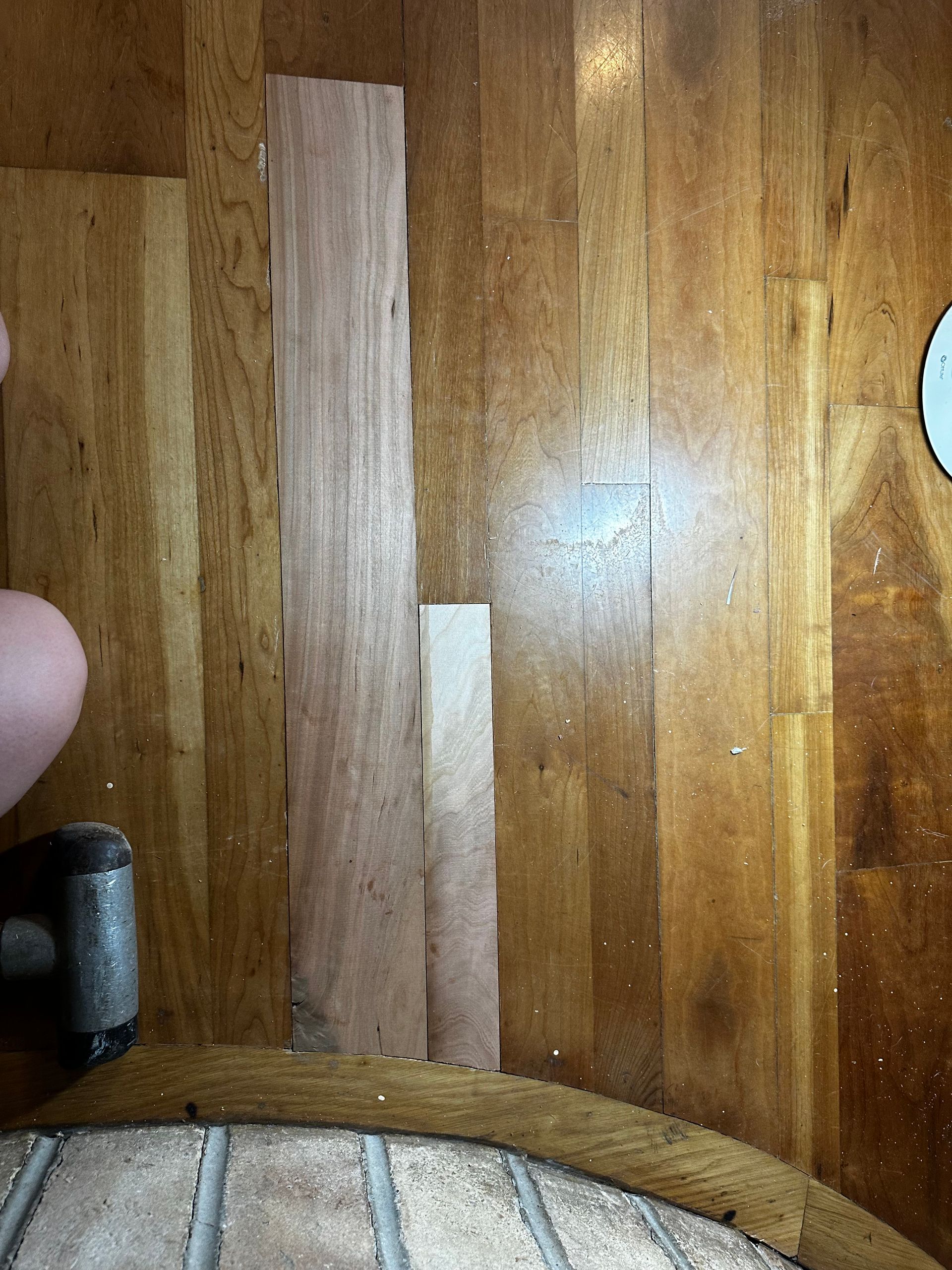 A person is hammering a piece of wood on a wooden floor.