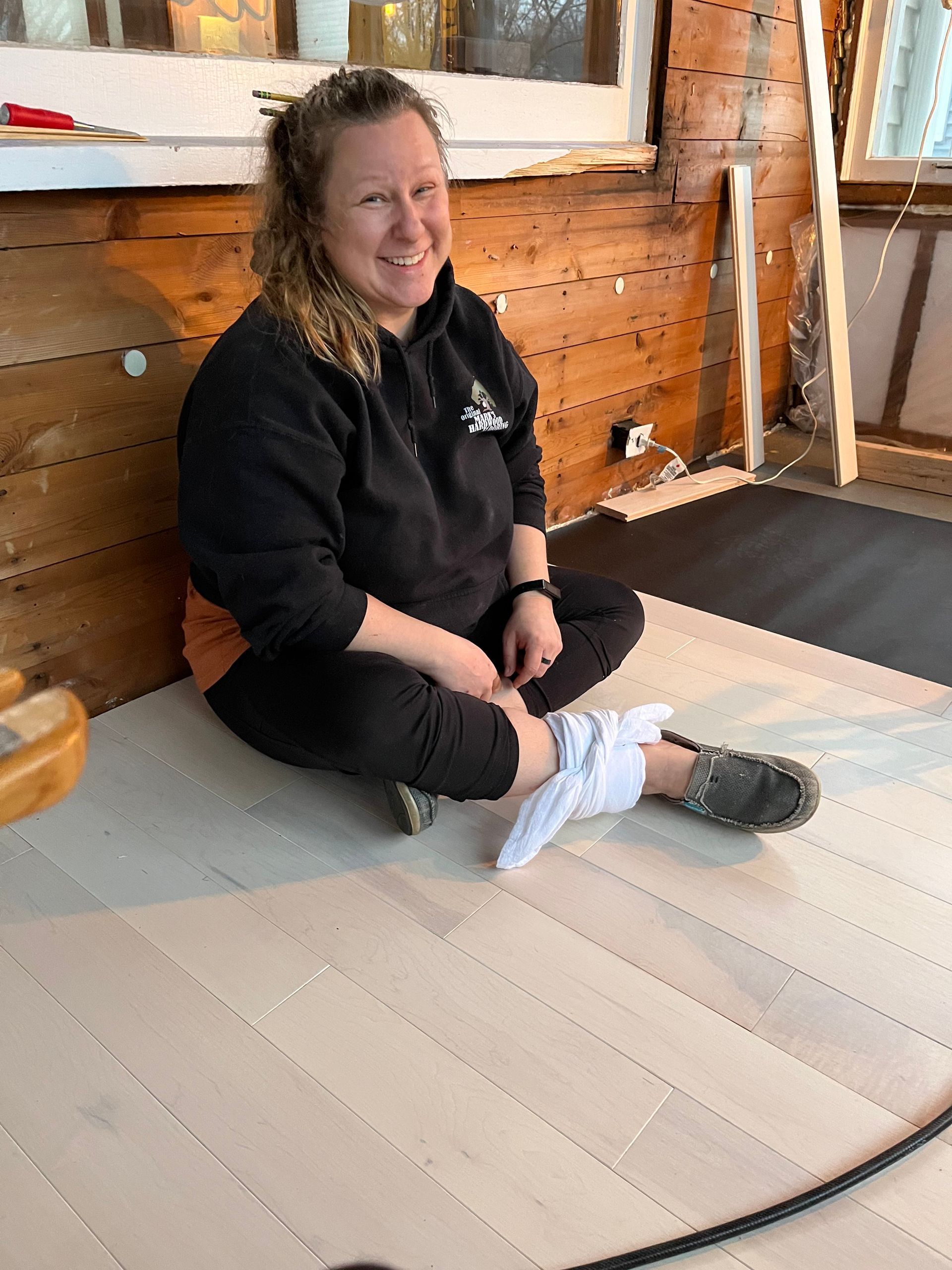 A woman is sitting on the floor with her legs crossed and smiling.
