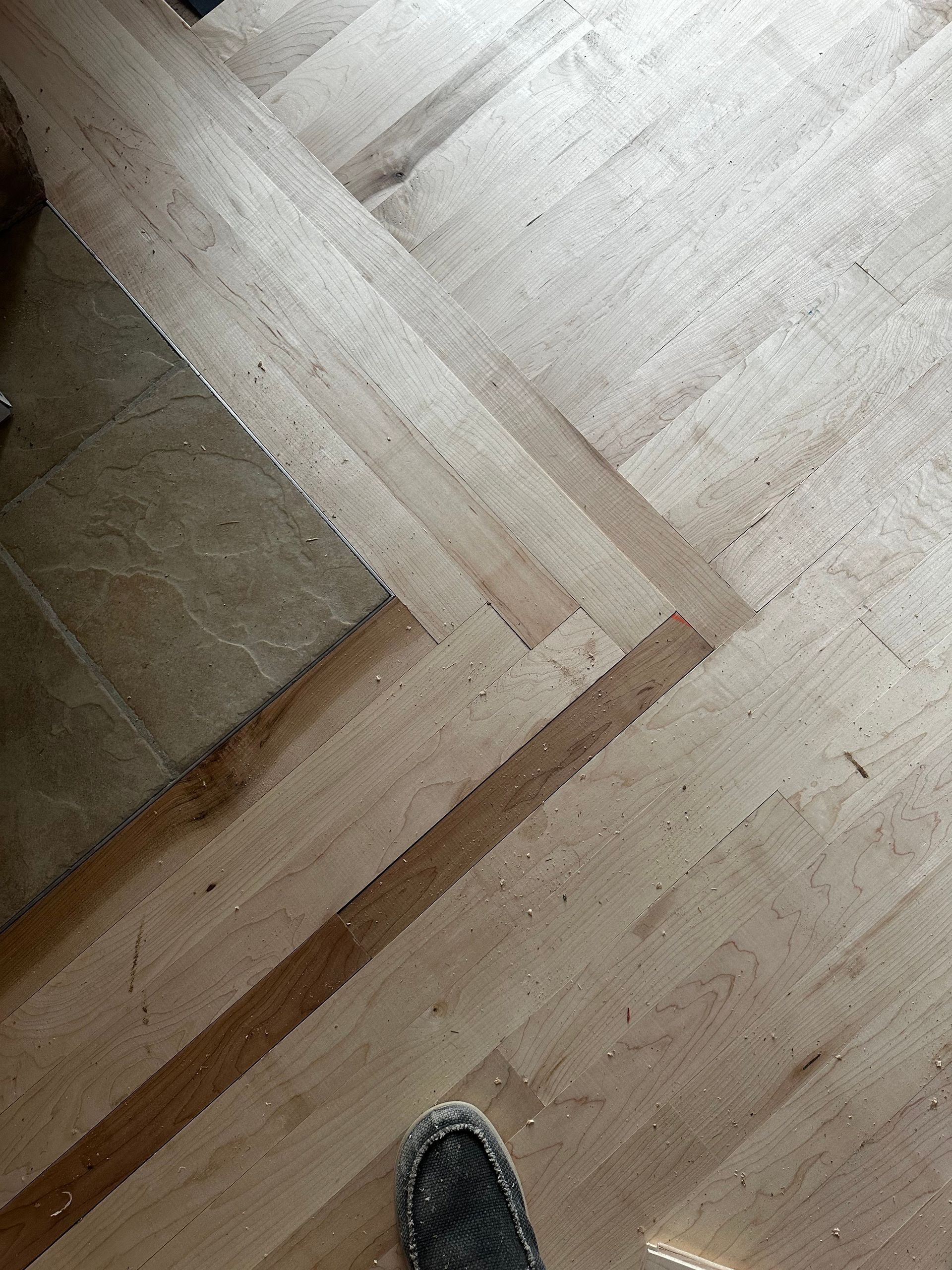 A person 's foot is standing on a wooden floor next to stairs.