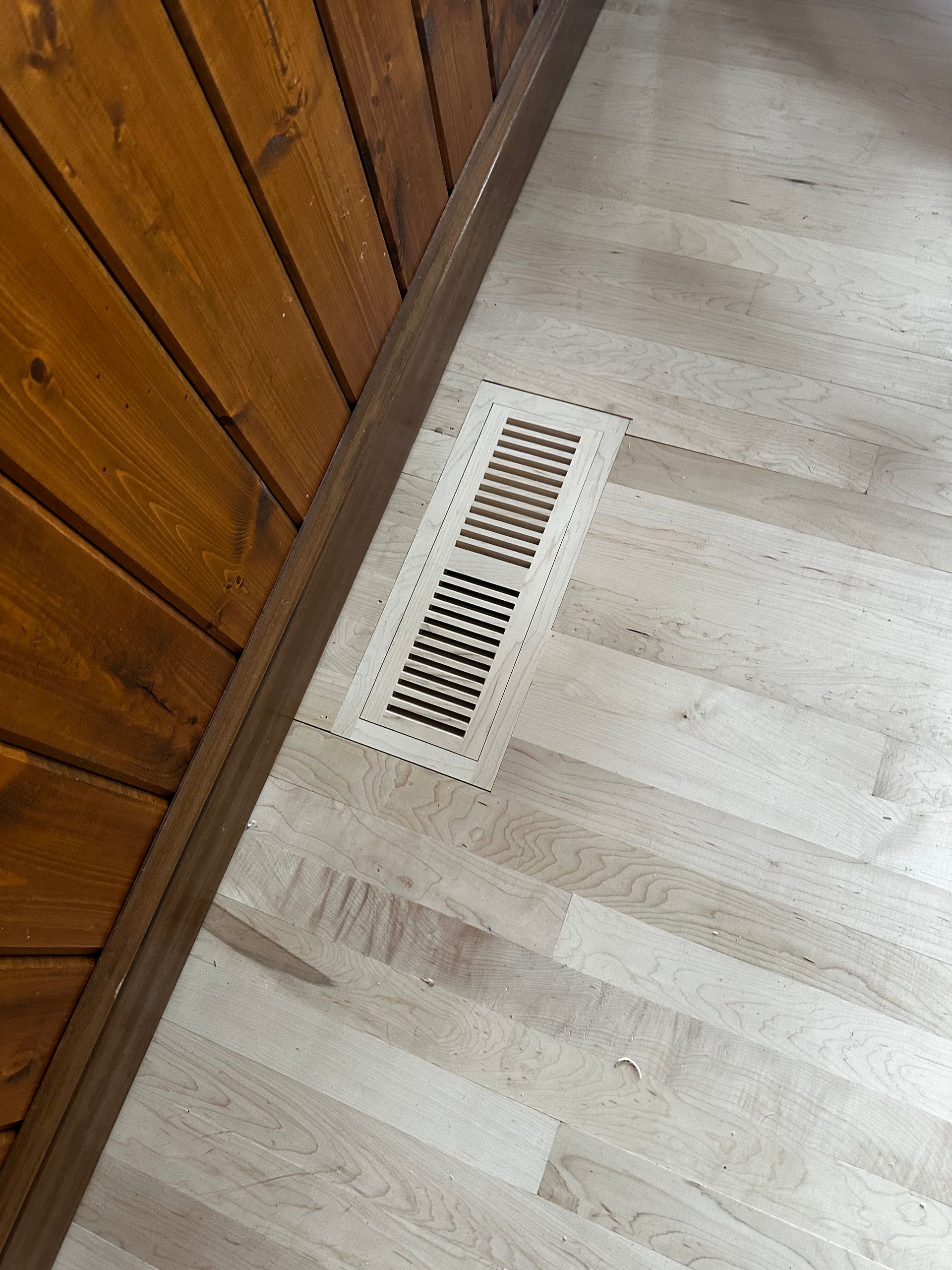 There is a vent on the floor next to a wooden wall.