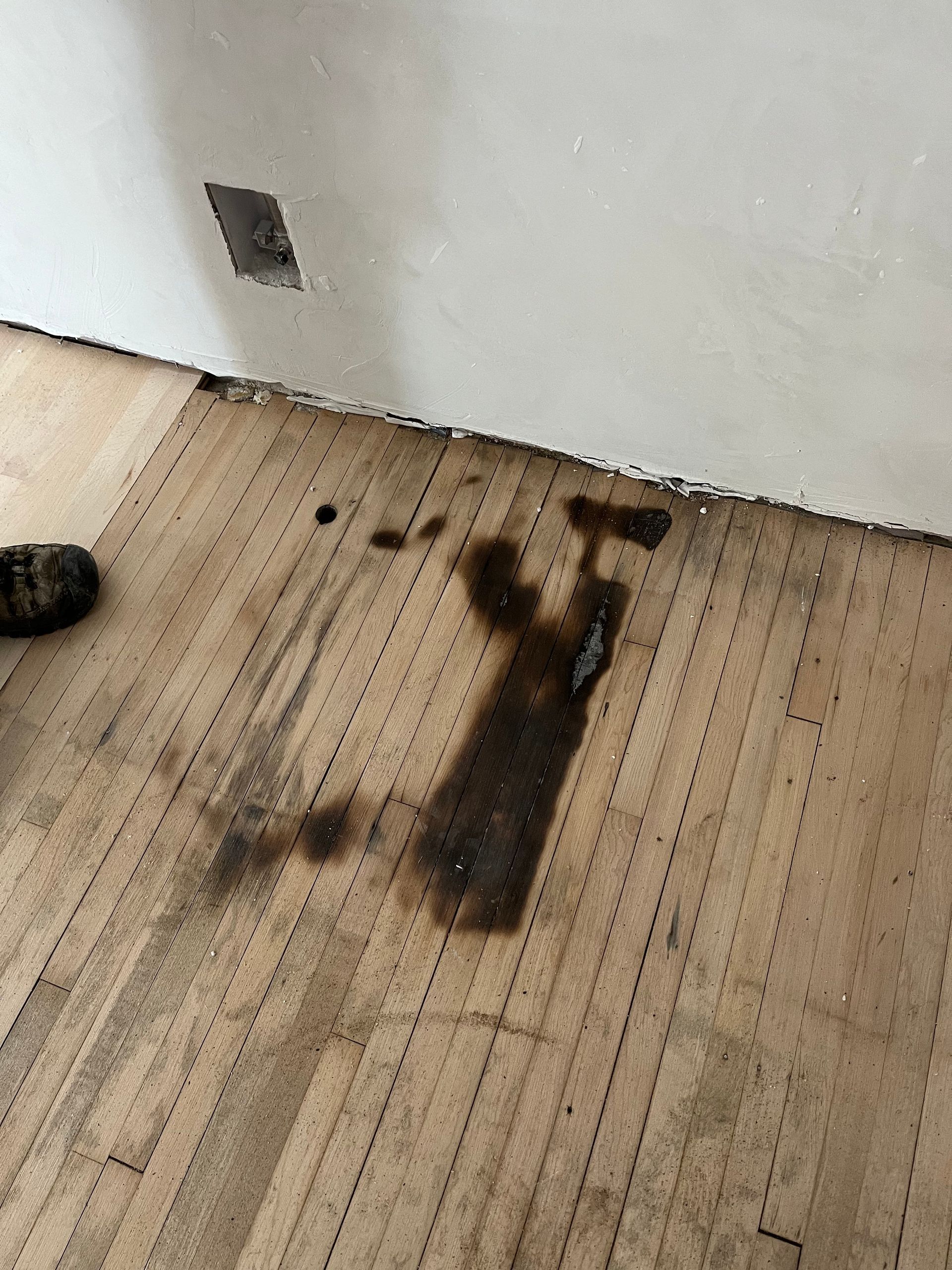 A person is standing on a wooden floor with a stain on it.