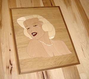 A wooden painting of marilyn monroe is sitting on a wooden floor.