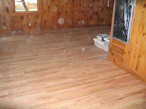 A wooden floor in a room with wood paneling and a fireplace.