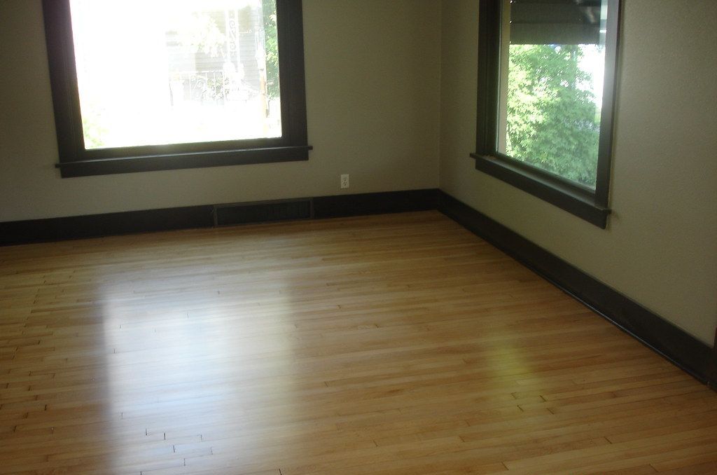 An empty room with hardwood floors and two windows