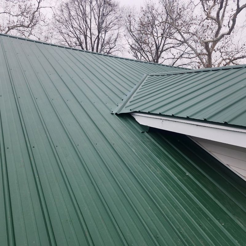 A green metal roof on a house with trees in the background.