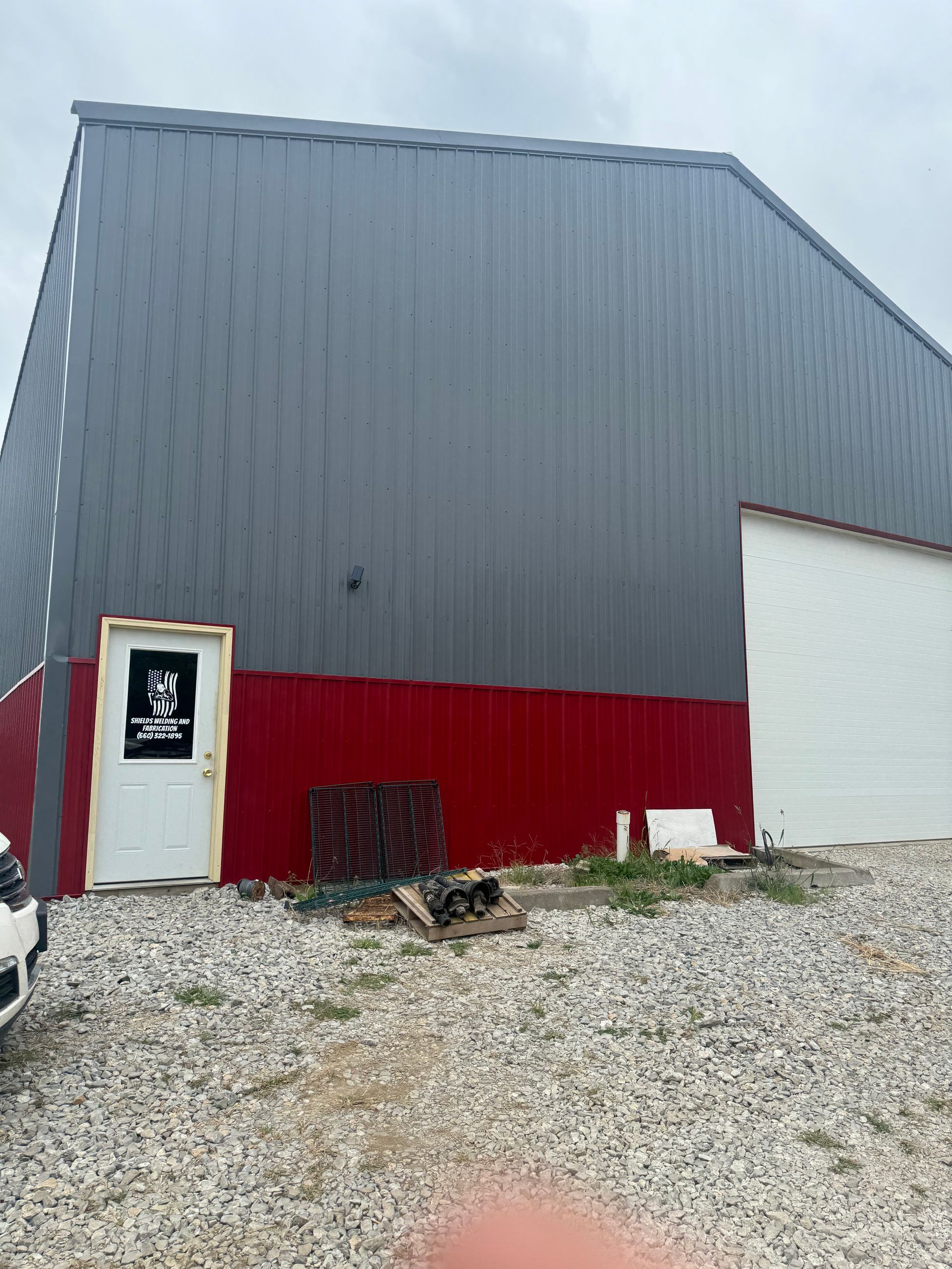 A red and gray building with a white door is sitting on top of a gravel lot.