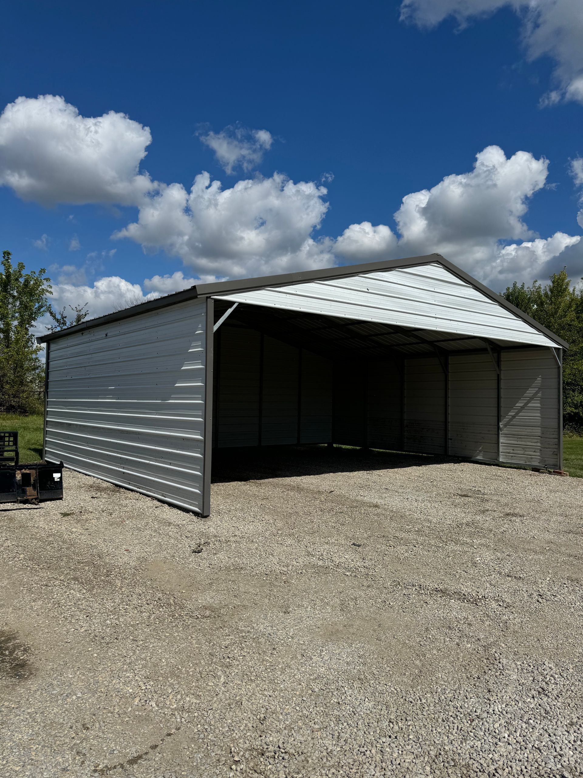 A large white metal building is sitting on top of a gravel lot.