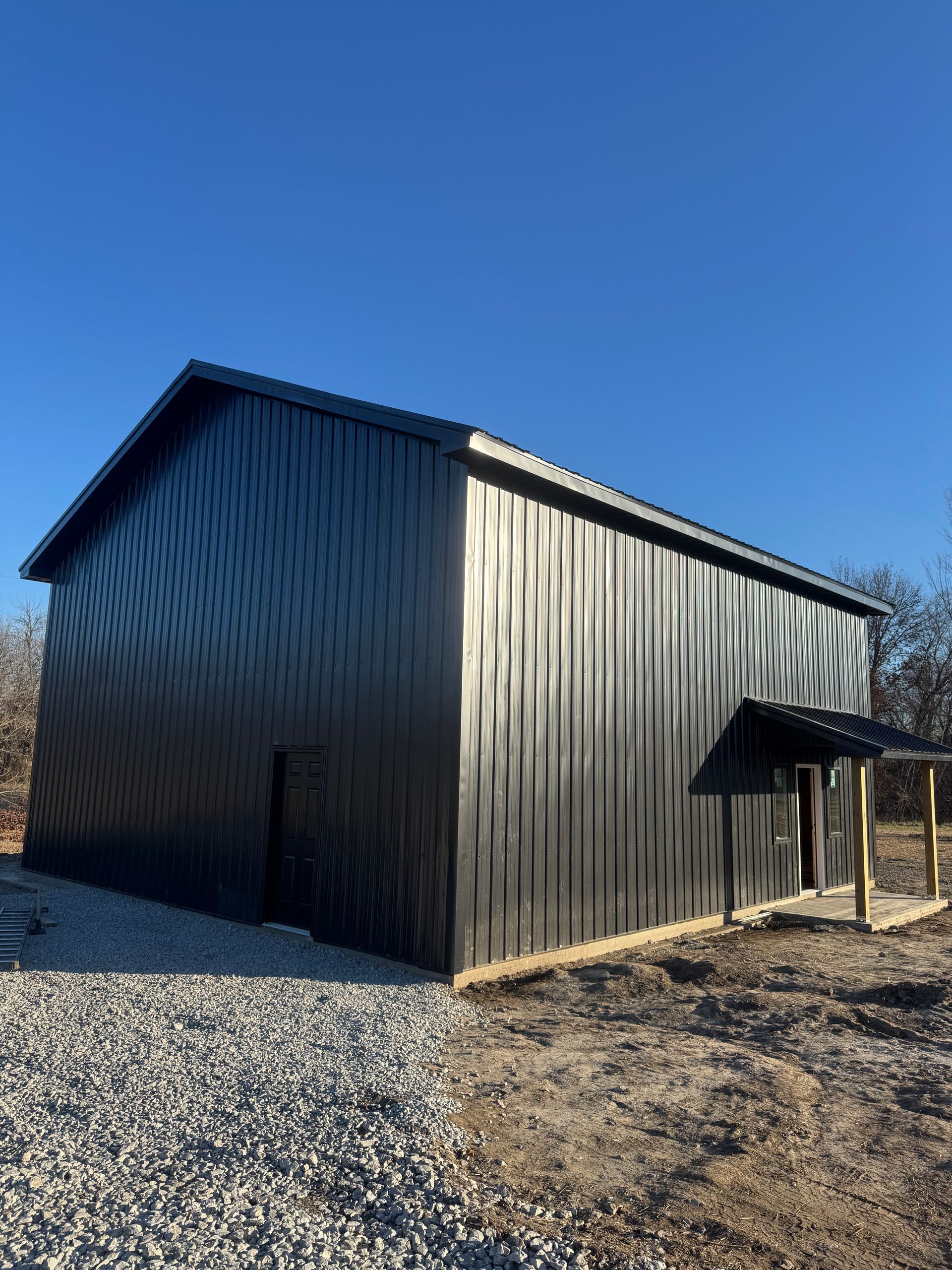 A large black metal building is sitting on top of a gravel lot.