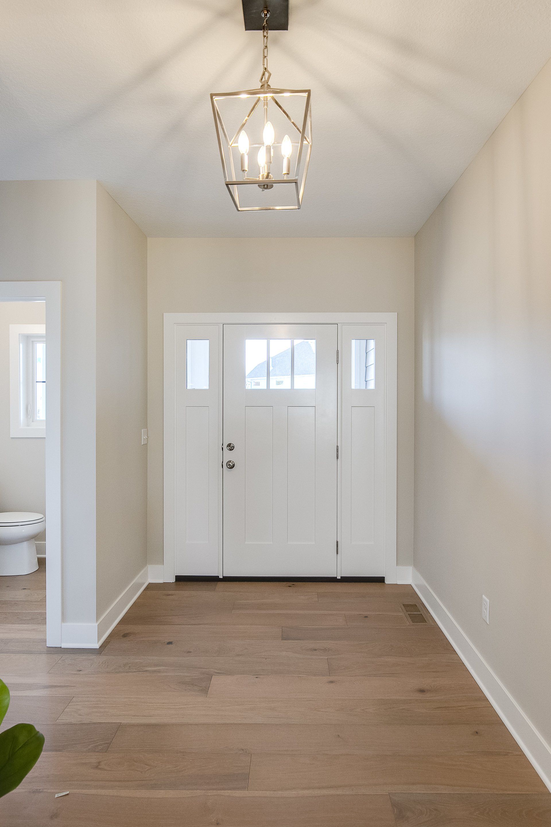 A hallway with a white door and a chandelier hanging from the ceiling.