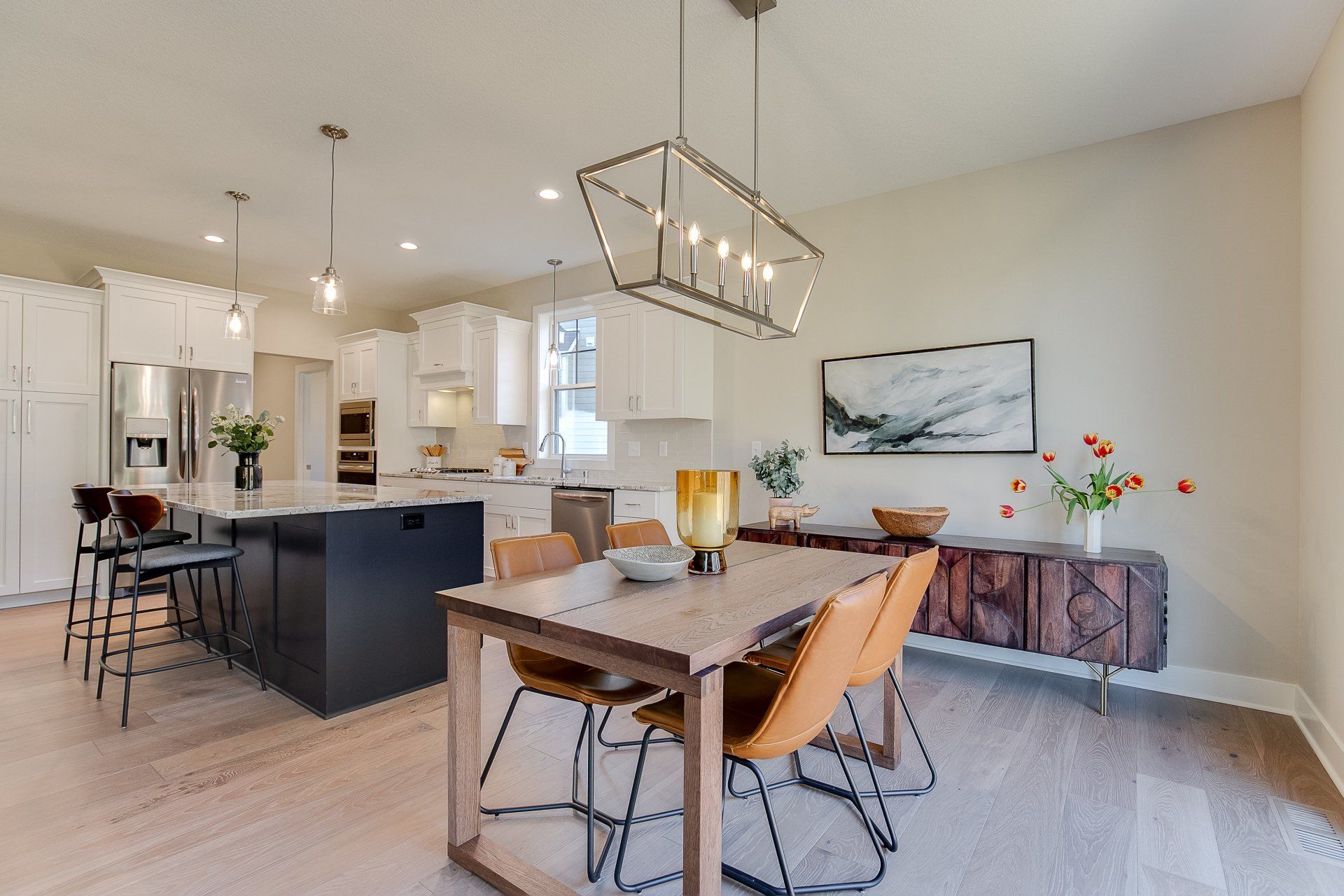 A dining room with a table and chairs and a kitchen in the background.