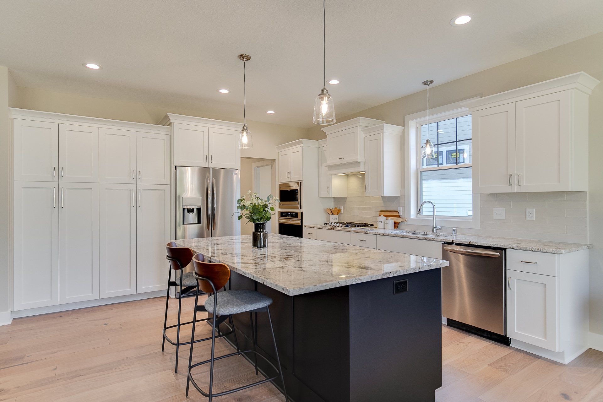 A kitchen with white cabinets,  granite countertops, stainless steel appliances, and a large island.