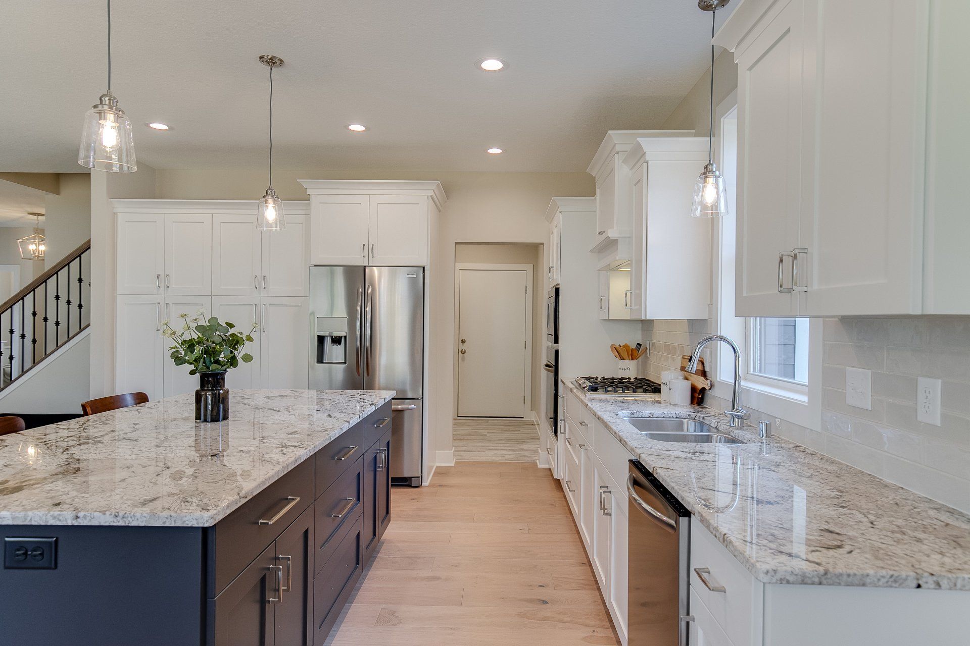 A kitchen with white cabinets, granite countertops, stainless steel appliances, and a large island.
