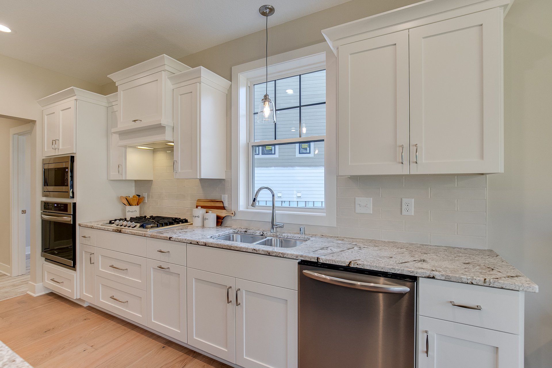 A kitchen with white cabinets, granite countertops, stainless steel appliances, and a window.