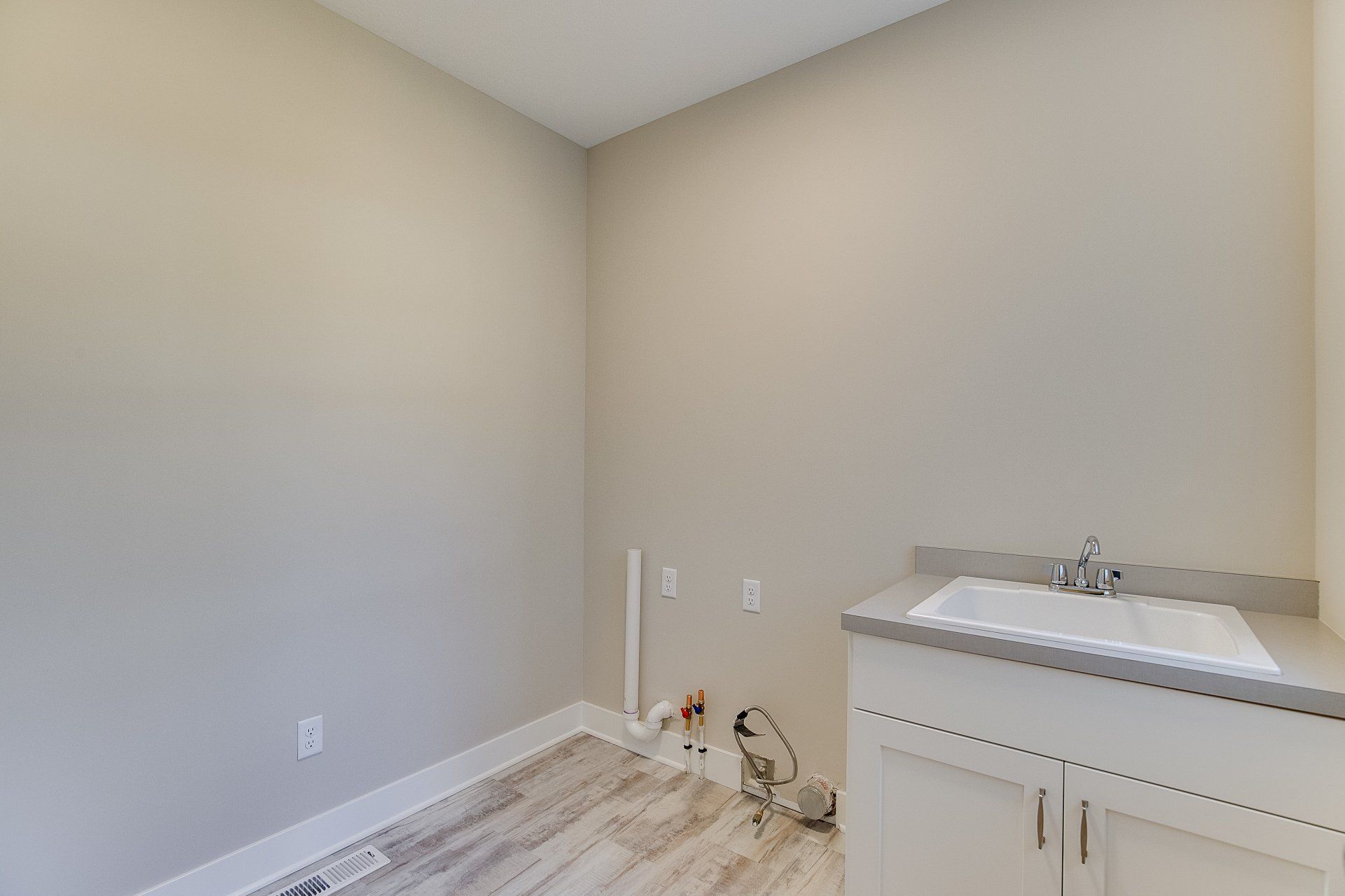 An empty laundry room with a sink and cabinets.