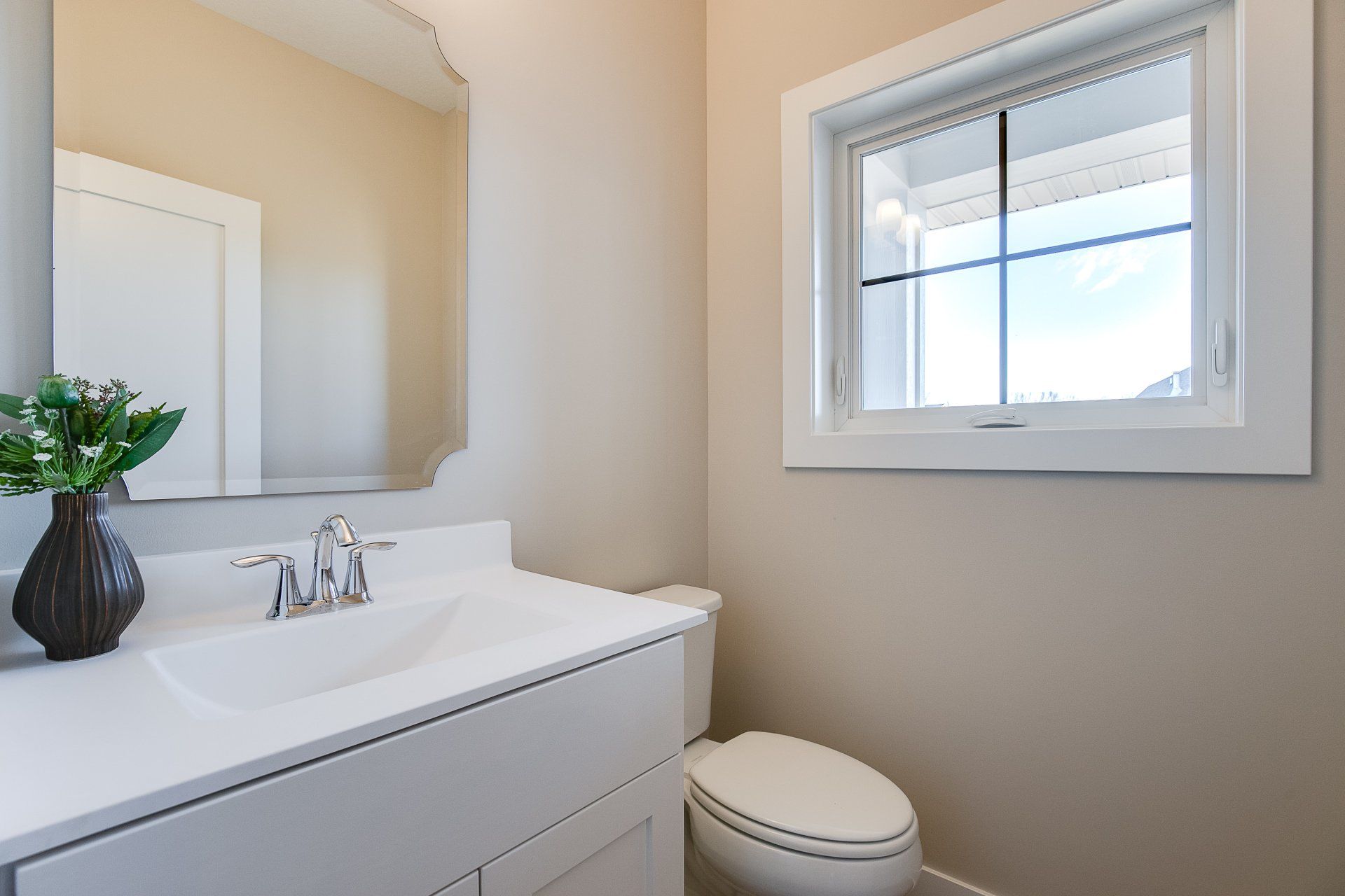 A bathroom with a sink, toilet, mirror, and window.
